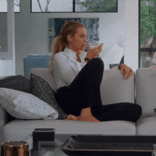 a woman sits on a couch with her legs crossed and looks at her phone