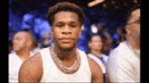 a man wearing a white tank top and a necklace is sitting in a stadium .