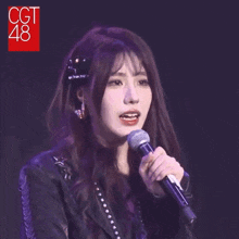 a girl singing into a microphone with a cgt 48 logo in the background