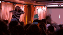 a woman in a striped sweater is dancing in front of a crowd of people