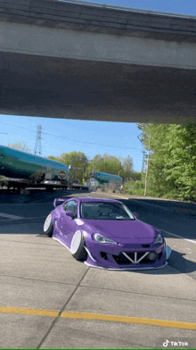 a purple car is parked underneath a bridge with a train in the background