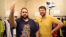 two men are standing next to each other in front of a row of clothes .