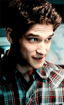 a close up of a young man wearing a plaid shirt and smiling
