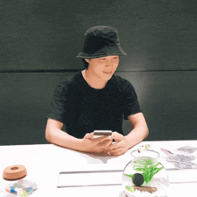 a man in a black hat is sitting at a table looking at his phone