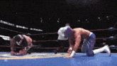 two wrestlers are kneeling down in a wrestling ring with the letter x on the bottom right corner .