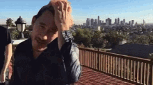 a man wipes his forehead with his hand on a balcony overlooking a city