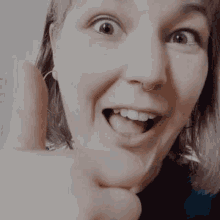 a close up of a woman giving a thumbs up sign with her mouth open .