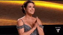 a woman in a dress is clapping her hands in front of a screen that says en vivo .