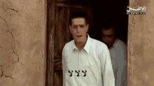 a man in a white shirt is standing in front of a door with arabic writing on it