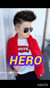 a little boy wearing sunglasses and a red jacket with the word hero on it .