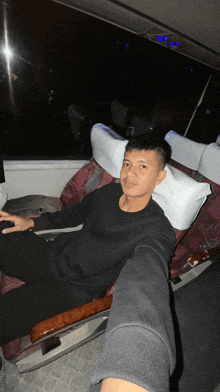 a young man in a black shirt sits in a chair with a white pillow on his head