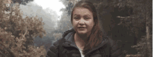 a woman in a black jacket is smiling in front of trees and the word wex is on the bottom right