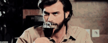 a man with a beard is drinking a glass of wine from a glass .