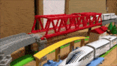 a toy train is going under a red bridge on a track .