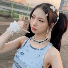 a woman wearing a blue tank top and a necklace is giving a thumbs up sign