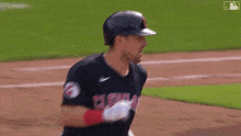a baseball player wearing a helmet and a cleveland uniform is running on the field .