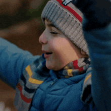 a young boy wearing a knitted hat and gloves holds his nose
