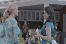 two women are standing next to each other at a party and talking .