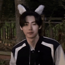 a young man wearing bunny ears and a black and white jacket is standing in the woods .