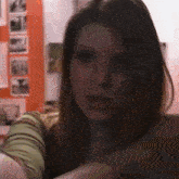 a close up of a woman 's face in a dark room with pictures on the wall behind her