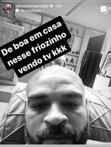 a black and white photo of a man with a caption that says de boa em casa nesse friozinho vendo tv kkk