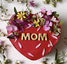 a red heart shaped cake with the word mom in gold letters