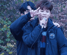 a man in a bts jacket is holding a microphone and giving a peace sign