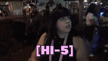 a woman in a black tank top says hi-5 while standing in a crowd