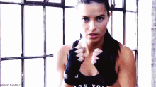 a woman wearing boxing gloves and a black tank top is standing in front of a window .