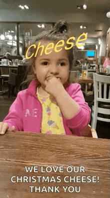 a little girl is sitting at a table with her hand in her mouth and the words " we love our christmas cheese thank you "