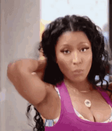 a woman in a purple tank top is looking at herself in a mirror .
