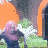 a woman with pink hair is standing in front of a large orange sign