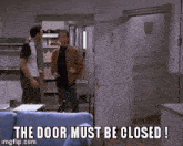 two men standing in front of a door with the words " the door must be closed "