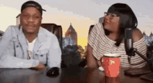 a man and a woman are sitting at a table talking into a microphone .
