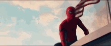 a man in a spiderman costume is sitting on top of a building with an american flag wrapped around his neck .