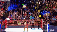 a woman is standing in a wrestling ring in front of a crowd while a referee watches .