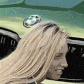 a woman with blonde hair is standing in front of a green bmw