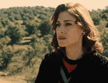 a woman with a serious look on her face stands in front of trees