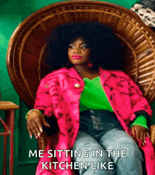 a woman in a pink jacket and green shirt is sitting in a wicker chair with the caption me sitting in the kitchen like