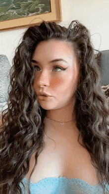 a woman with long curly hair is wearing a blue lace top