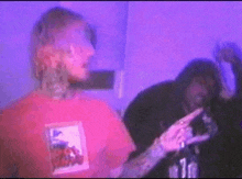 a man in a red shirt is standing next to a man in a black hoodie in a room with purple lights .