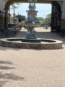 a fountain in a brick courtyard with tables and chairs behind it