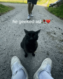 a black cat is sitting on the side of a road next to a person 's feet with the caption he geeked asl
