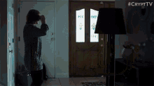 a woman is standing in front of a door with a lamp in front of her and the words #crypttv on the bottom