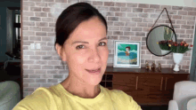 a woman in a yellow shirt is smiling in front of a brick wall
