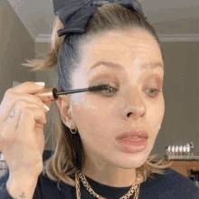 a woman is applying mascara to her eyelashes while wearing a headband .