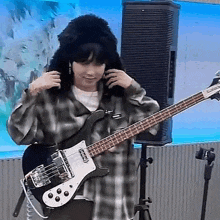 a woman in a plaid shirt is holding a bass guitar in front of a speaker .