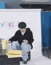 a man is sitting on a box with his legs crossed in front of a wall with the word kit on it