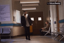 a man in a suit walks down a hallway next to a sign that says x7wickreddy
