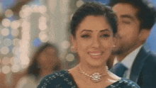 a close up of a woman wearing a necklace and smiling with a man in the background .